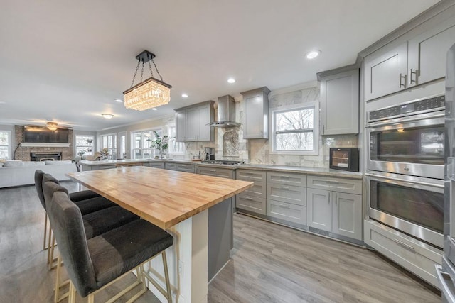 kitchen with wood counters, a kitchen breakfast bar, gray cabinetry, ornamental molding, and wall chimney range hood