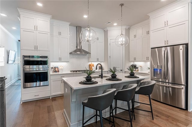 kitchen featuring an inviting chandelier, stainless steel appliances, dark hardwood / wood-style flooring, wall chimney range hood, and an island with sink