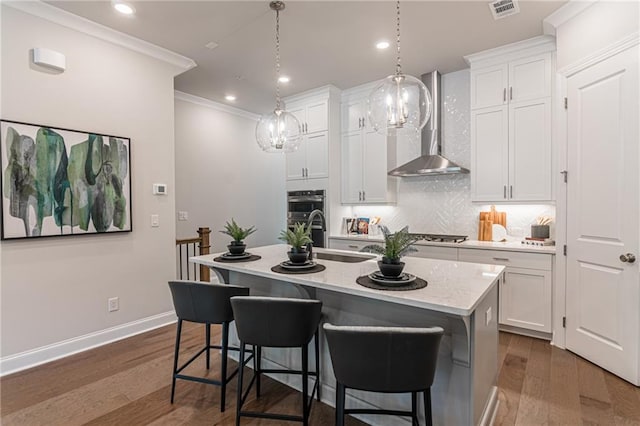 kitchen with decorative light fixtures, an island with sink, dark wood-type flooring, wall chimney exhaust hood, and white cabinets