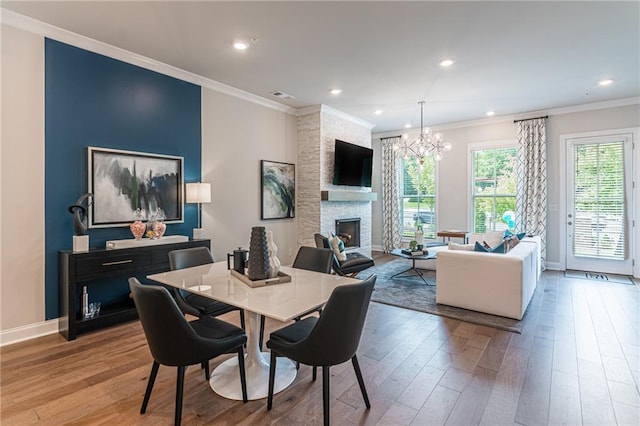 dining area featuring crown molding, hardwood / wood-style flooring, a notable chandelier, and a stone fireplace