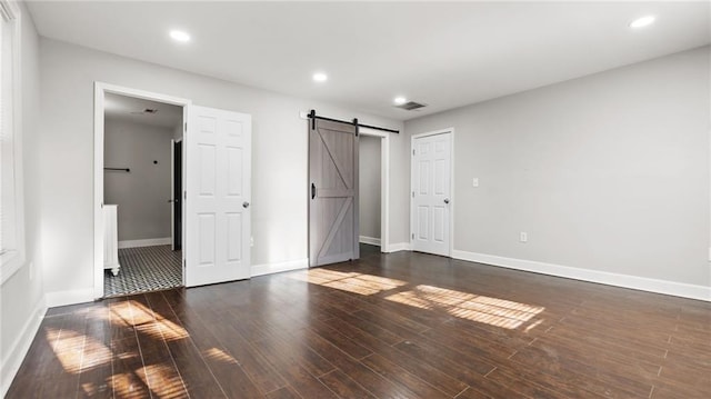 unfurnished bedroom with dark hardwood / wood-style floors and a barn door