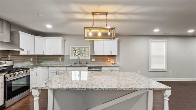 kitchen featuring wall chimney range hood, sink, hanging light fixtures, stainless steel appliances, and white cabinets