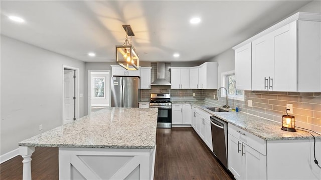 kitchen featuring wall chimney exhaust hood, sink, white cabinetry, appliances with stainless steel finishes, and pendant lighting