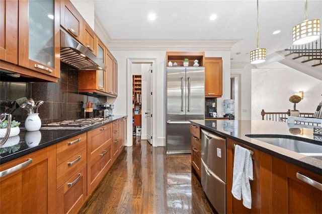 kitchen featuring brown cabinetry, decorative backsplash, appliances with stainless steel finishes, crown molding, and under cabinet range hood