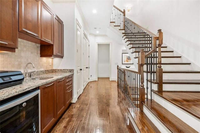 kitchen featuring dark wood finished floors, tasteful backsplash, a sink, light stone countertops, and beverage cooler