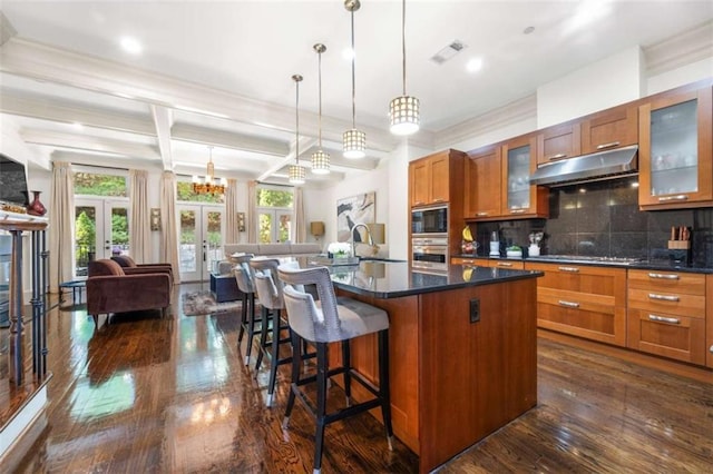 kitchen featuring french doors, appliances with stainless steel finishes, brown cabinetry, open floor plan, and under cabinet range hood