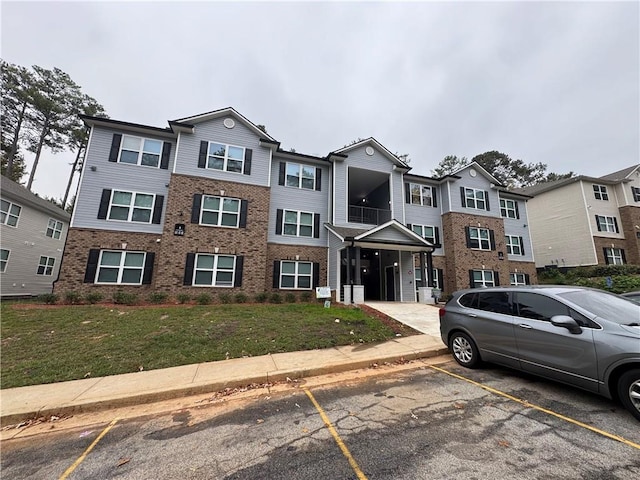 view of property with uncovered parking, brick siding, and a front lawn