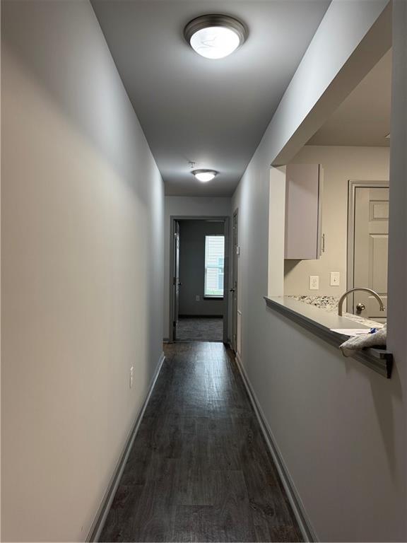 corridor with dark wood-style floors, a sink, and baseboards