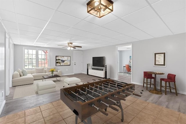 living room with tile patterned floors, ceiling fan, a paneled ceiling, and baseboards