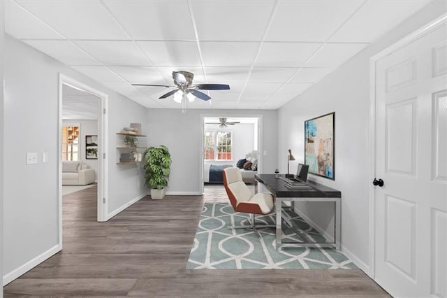 home office featuring a paneled ceiling, baseboards, wood finished floors, and ceiling fan