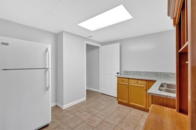 kitchen featuring light tile patterned floors, baseboards, a sink, freestanding refrigerator, and brown cabinetry