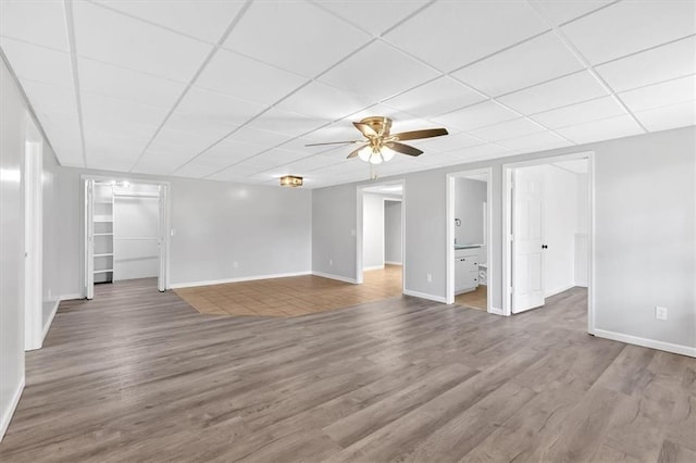 unfurnished living room featuring a paneled ceiling, wood finished floors, ceiling fan, and baseboards