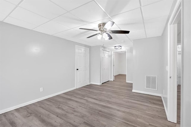 empty room with a paneled ceiling, ceiling fan, visible vents, wood finished floors, and baseboards