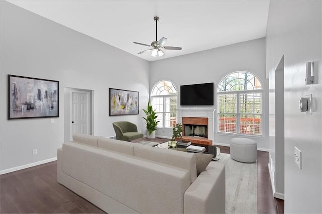 living area featuring ceiling fan, baseboards, dark wood finished floors, and a fireplace