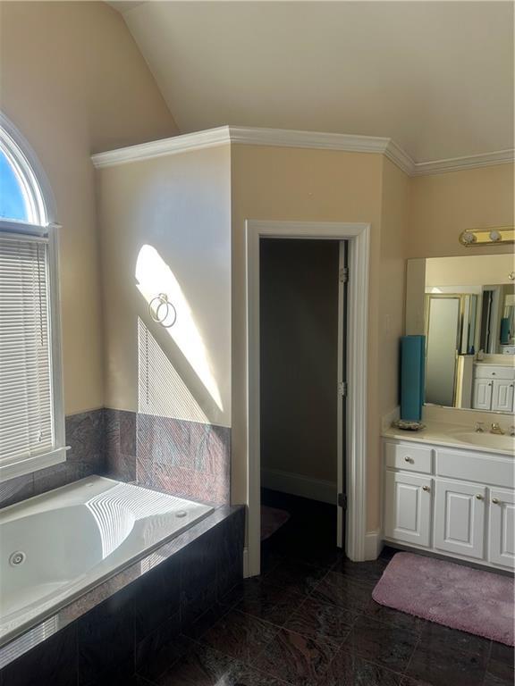 bathroom featuring ornamental molding, vanity, lofted ceiling, and tiled tub