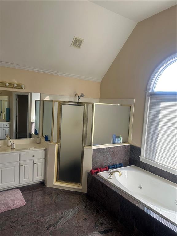 bathroom featuring vanity, independent shower and bath, and vaulted ceiling