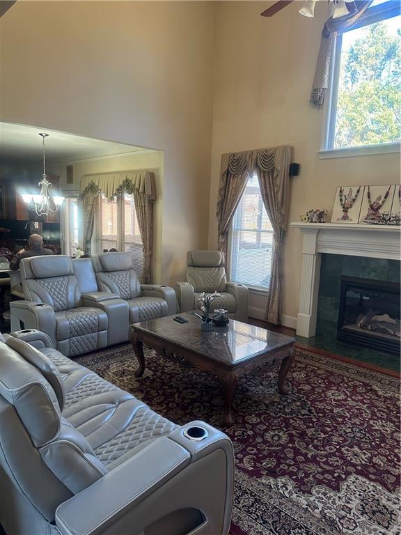 living room featuring ceiling fan with notable chandelier, wood-type flooring, a high ceiling, and a tiled fireplace