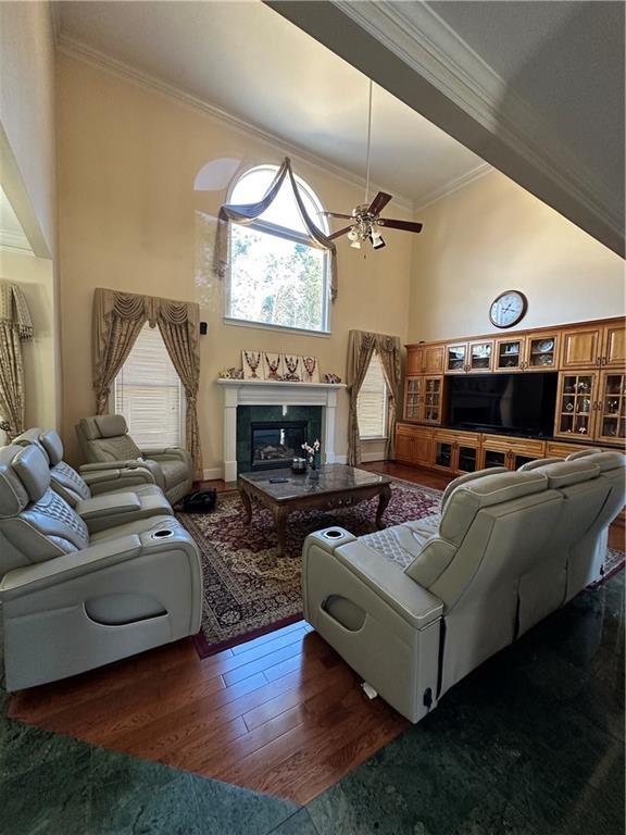 living room with crown molding, a towering ceiling, dark wood-type flooring, and ceiling fan