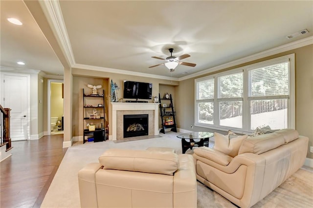 living room featuring ceiling fan, a tiled fireplace, ornamental molding, and hardwood / wood-style floors