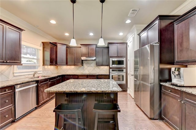 kitchen featuring hanging light fixtures, appliances with stainless steel finishes, a breakfast bar, sink, and a center island