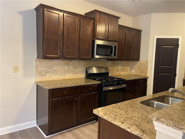 kitchen with dark brown cabinetry, sink, black gas range, and light wood-type flooring