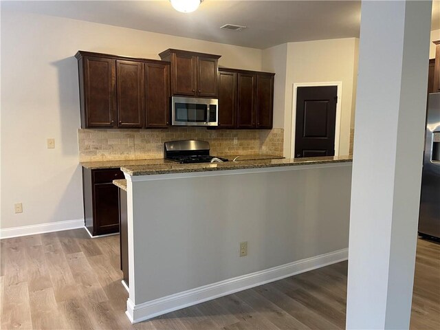 kitchen featuring stainless steel appliances, stone countertops, light hardwood / wood-style floors, and kitchen peninsula