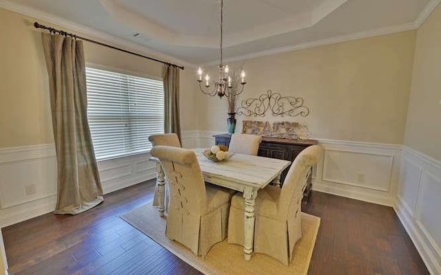 dining space featuring dark wood-type flooring, a tray ceiling, a chandelier, and crown molding