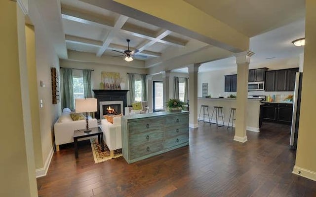 living room featuring ornate columns, coffered ceiling, ceiling fan, dark wood-type flooring, and beam ceiling