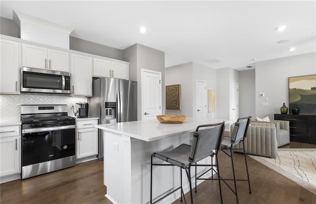 kitchen with a center island, dark wood-type flooring, white cabinets, appliances with stainless steel finishes, and a kitchen bar