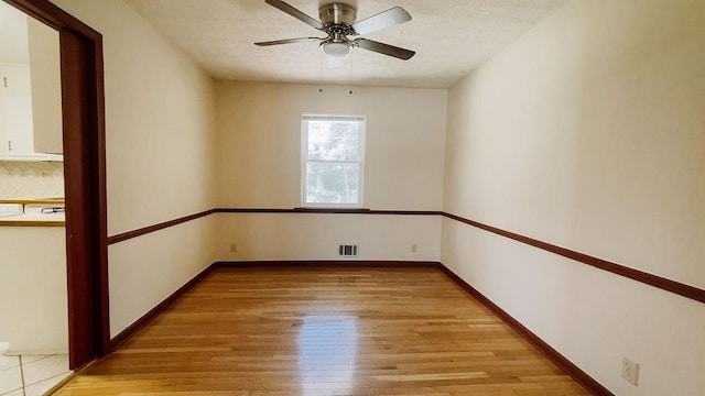 spare room featuring baseboards, a textured ceiling, light wood-style floors, ceiling fan, and visible vents