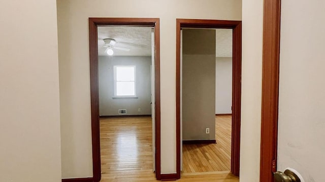 hall with baseboards, a textured ceiling, visible vents, and light wood finished floors
