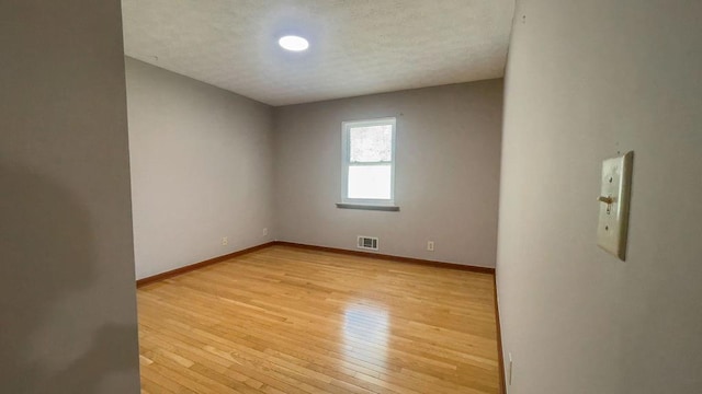 unfurnished room featuring a textured ceiling, baseboards, light wood finished floors, and visible vents