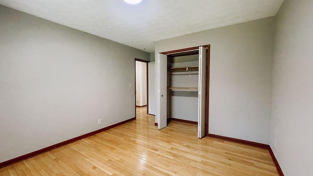 unfurnished bedroom featuring baseboards, a closet, and light wood-style flooring