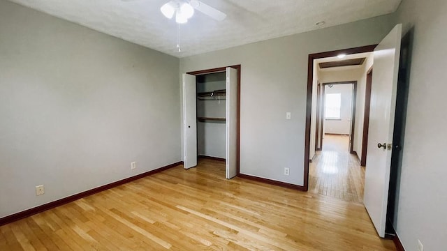 unfurnished bedroom featuring attic access, baseboards, light wood-style floors, and a ceiling fan