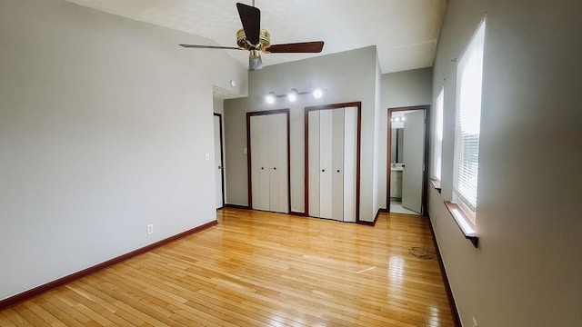 unfurnished bedroom featuring baseboards, light wood-type flooring, high vaulted ceiling, and two closets