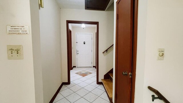 corridor featuring light tile patterned flooring, baseboards, and stairway