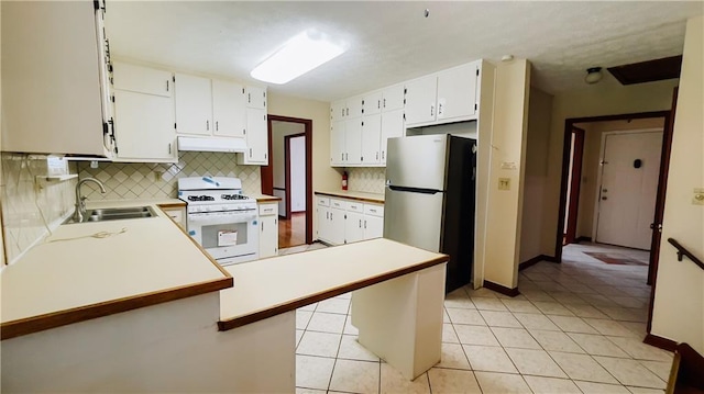 kitchen featuring gas range gas stove, under cabinet range hood, a sink, light tile patterned flooring, and freestanding refrigerator