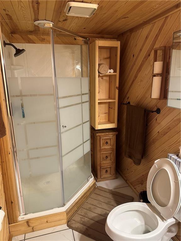 bathroom featuring visible vents, toilet, wood walls, a shower stall, and wooden ceiling