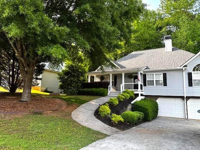 view of front of property with a chimney, driveway, covered porch, a garage, and roof with shingles