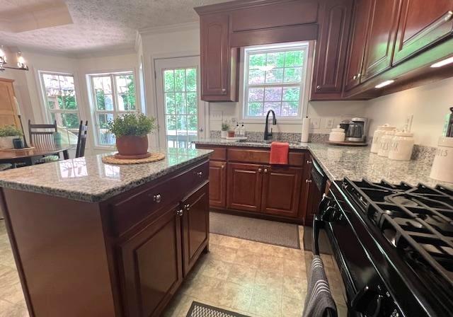 kitchen featuring a sink, light stone counters, a textured ceiling, a center island, and ornamental molding