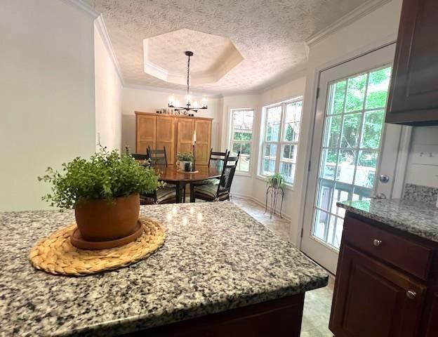 dining space with ornamental molding, a chandelier, a textured ceiling, and a raised ceiling