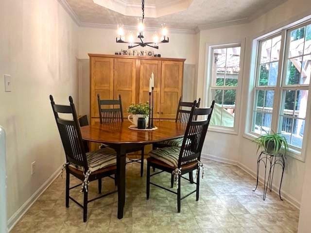 dining area with crown molding, healthy amount of natural light, a chandelier, baseboards, and a raised ceiling