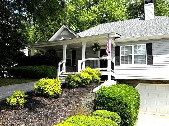 view of front of home featuring an attached garage, a chimney, a porch, roof with shingles, and driveway