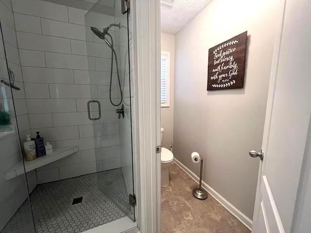 bathroom with a shower stall, toilet, a textured ceiling, and baseboards