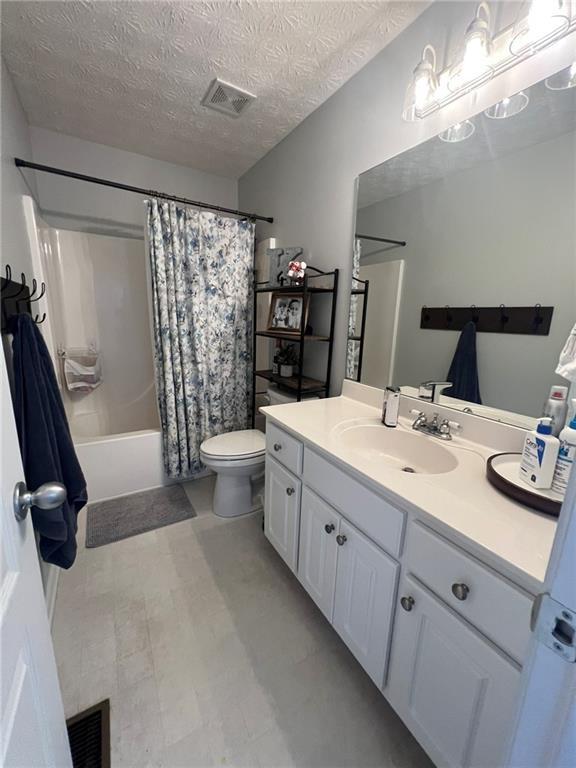 bathroom featuring toilet, shower / bath combo, vanity, a textured ceiling, and tile patterned floors