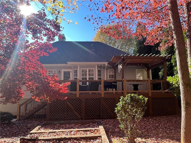back of property featuring a shingled roof, a deck, a vegetable garden, and a pergola