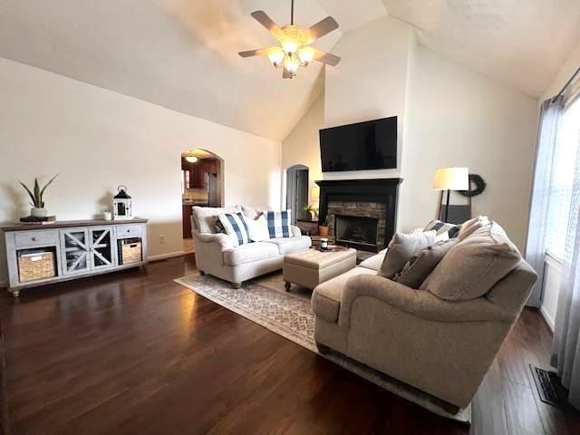 living room featuring arched walkways, ceiling fan, a fireplace, dark wood-type flooring, and high vaulted ceiling