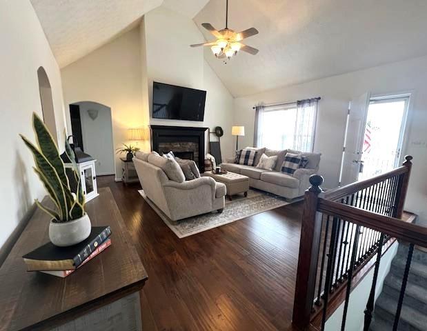 living room featuring arched walkways, a ceiling fan, wood finished floors, a fireplace, and high vaulted ceiling