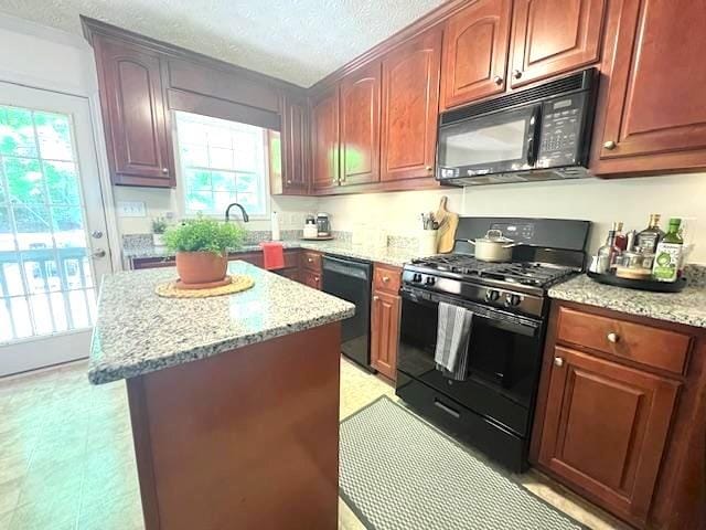 kitchen with black appliances, plenty of natural light, light stone countertops, a center island, and a textured ceiling
