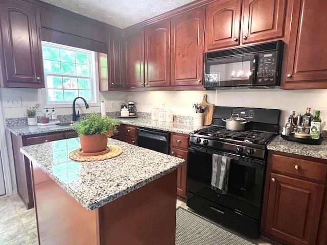 kitchen featuring black appliances, a sink, light stone counters, a center island, and a textured ceiling